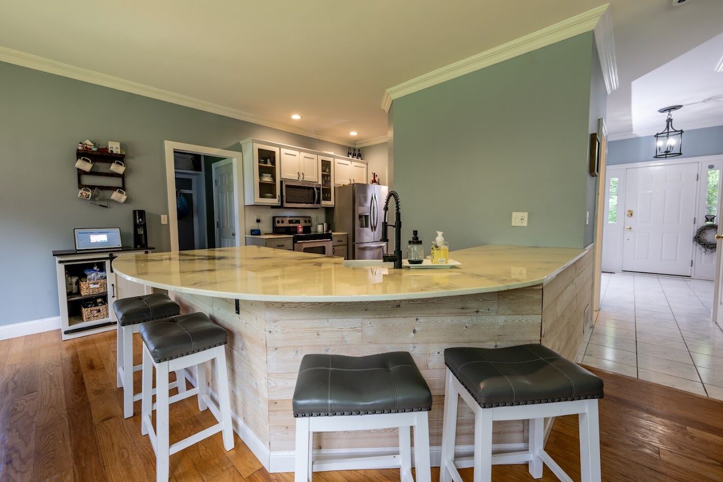 Curved reclaimed-wood bar with four leather stools, foyer visible beyond