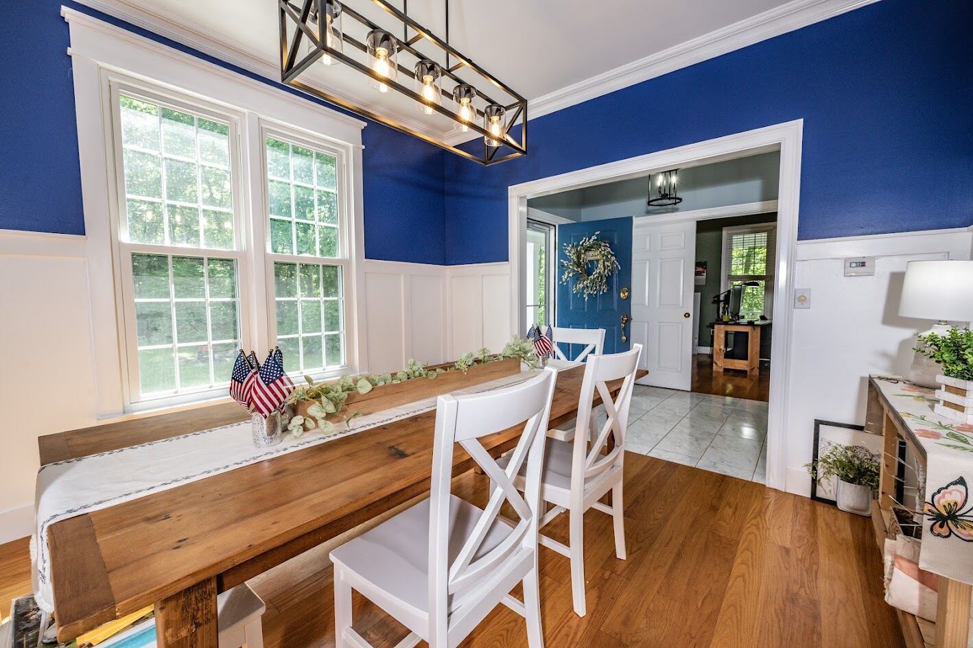 Formal dining room with deep blue walls, white wainscoting, and a reclaimed-wood farm table