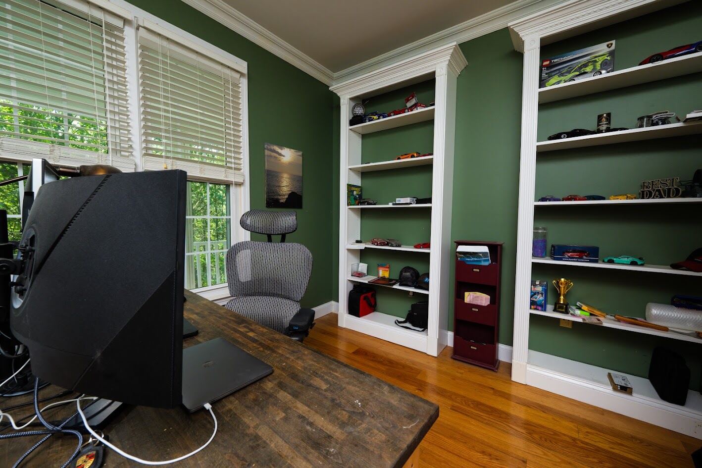 Private office with forest green walls, floor-to-ceiling white built-in bookshelves, and hardwood floors