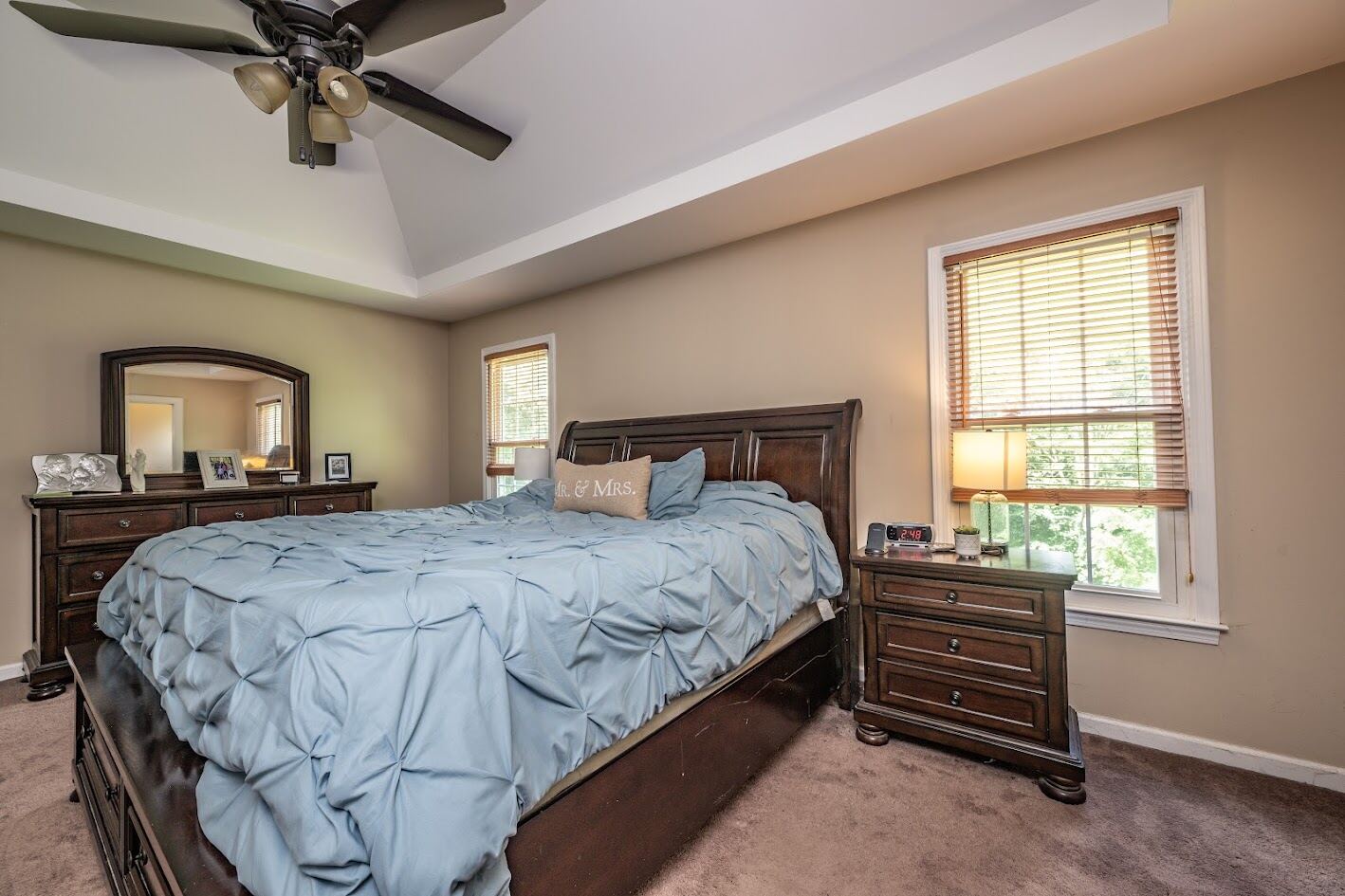 Primary bedroom with tray ceiling, ceiling fan, and windows on two walls